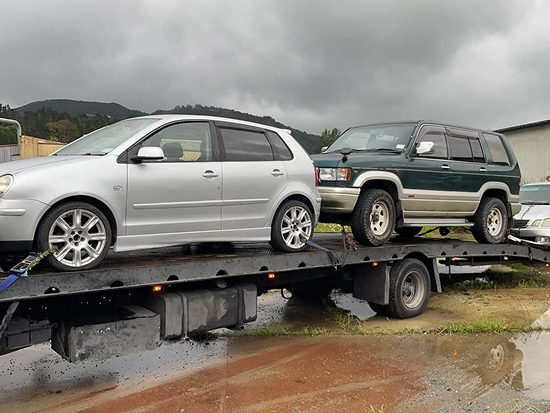 Tow truck transporting two scrap cars for removal in Whakatane